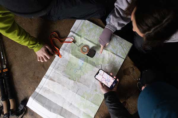 A group of people using the OS Maps app on a mobile and a paper map to plan a route